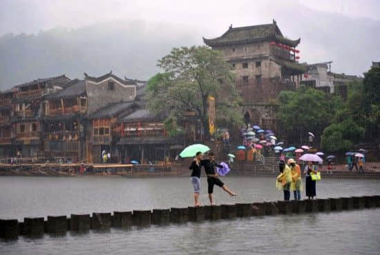 4月29日上午11时23分，几名游客冒雨在沱江跳岩上拍照。一场降雨让许多游客留在了酒店和客栈里。